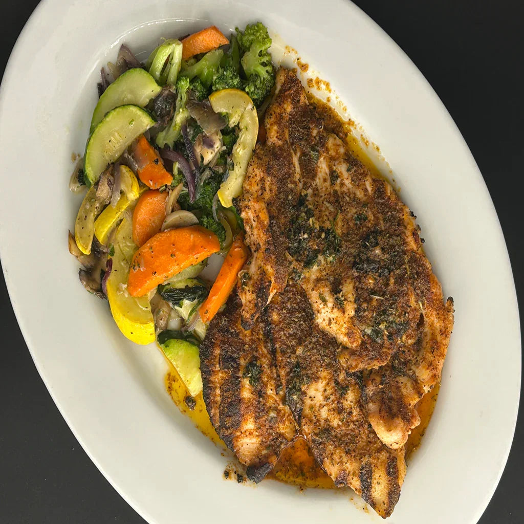 Plated dish of seasoned fish with a side of colorful vegetables on a white plate.